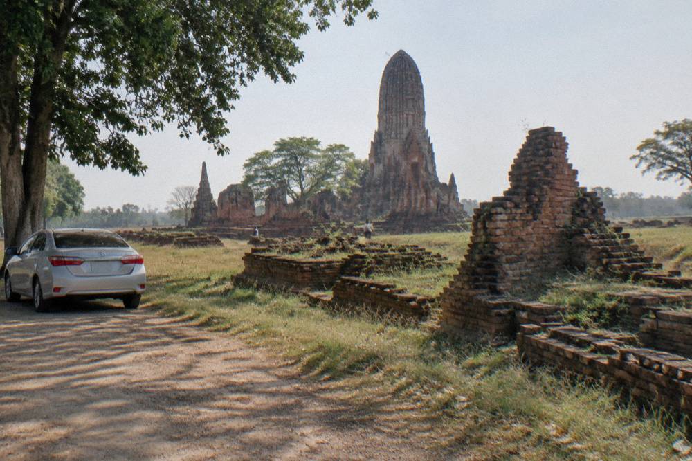 A private car parked on a quiet road beside ancient brick temple ruins