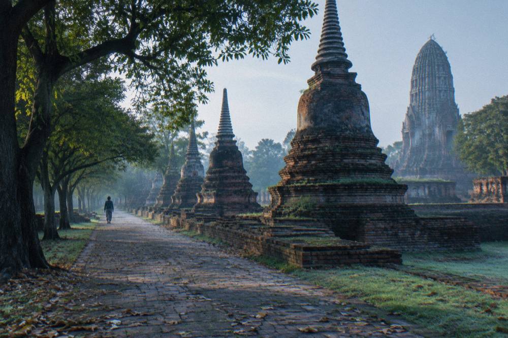 A row of old brick chedis beside a quiet tree-lined path on the Ayutthaya island