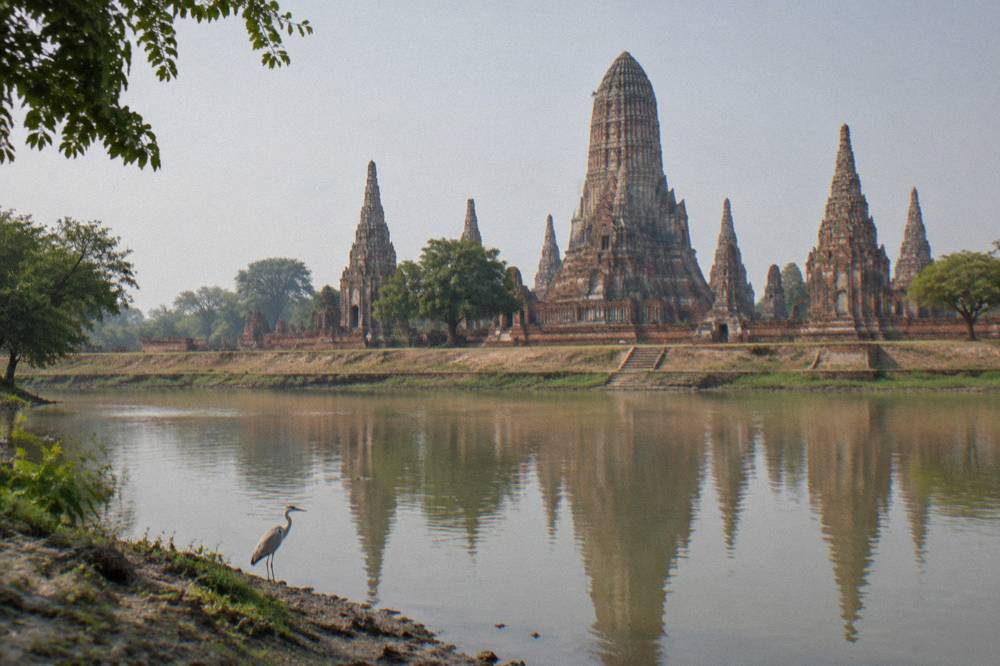 Tall laterite prang towers of an Ayutthaya temple reflected in still water at midday