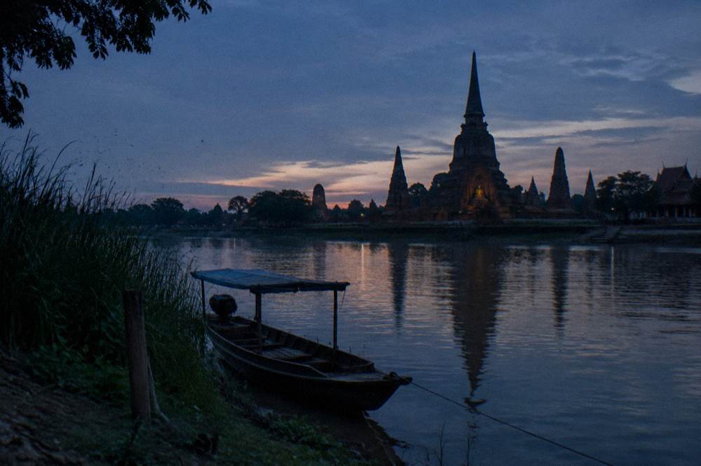 A quiet riverside bank at dusk with the silhouette of temple spires across the water