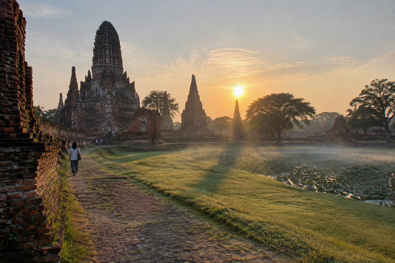 Ancient brick temple prangs of Ayutthaya standing in open grass under a bright morning sky