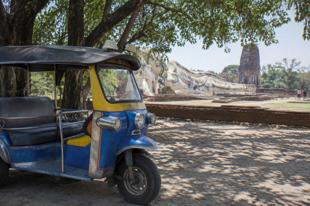 A decorated tuk tuk parked in the shade beside a temple wall