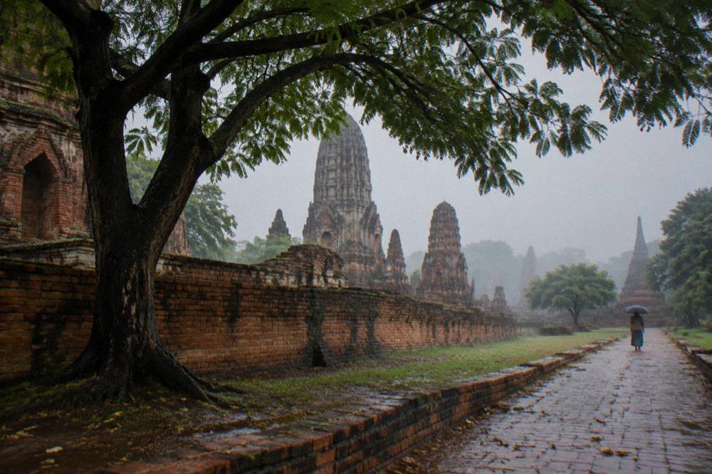 A tree-lined lane beside a red brick temple wall with bicycles leaning against it