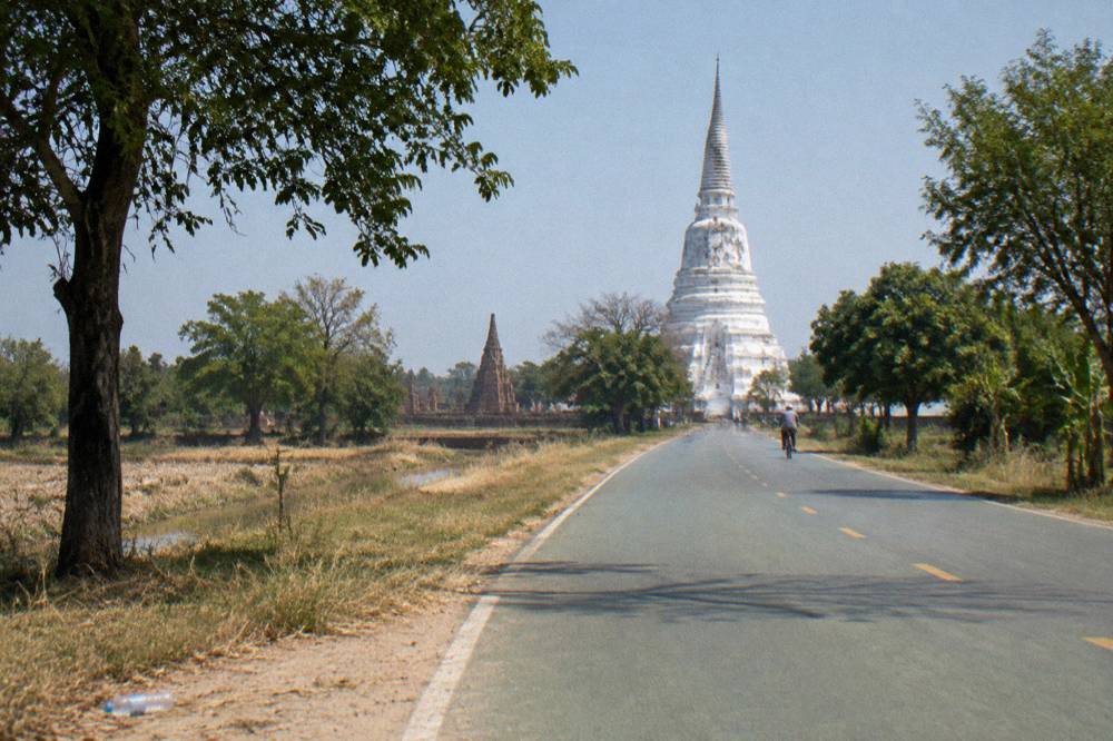 A quiet road through green countryside with a white stupa in the distance