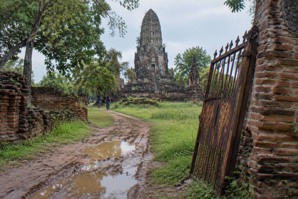A cyclist riding a bicycle path past ruined brick temple walls in Ayutthaya