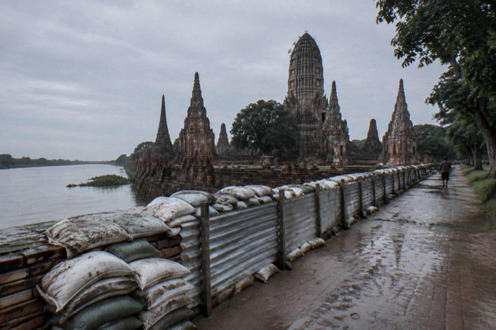 A flood barrier of sandbags and metal panels along a riverside temple wall