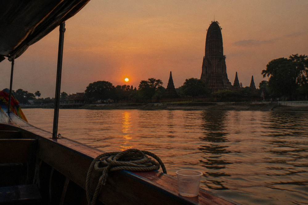 A temple prang silhouette against an orange sky above a calm river