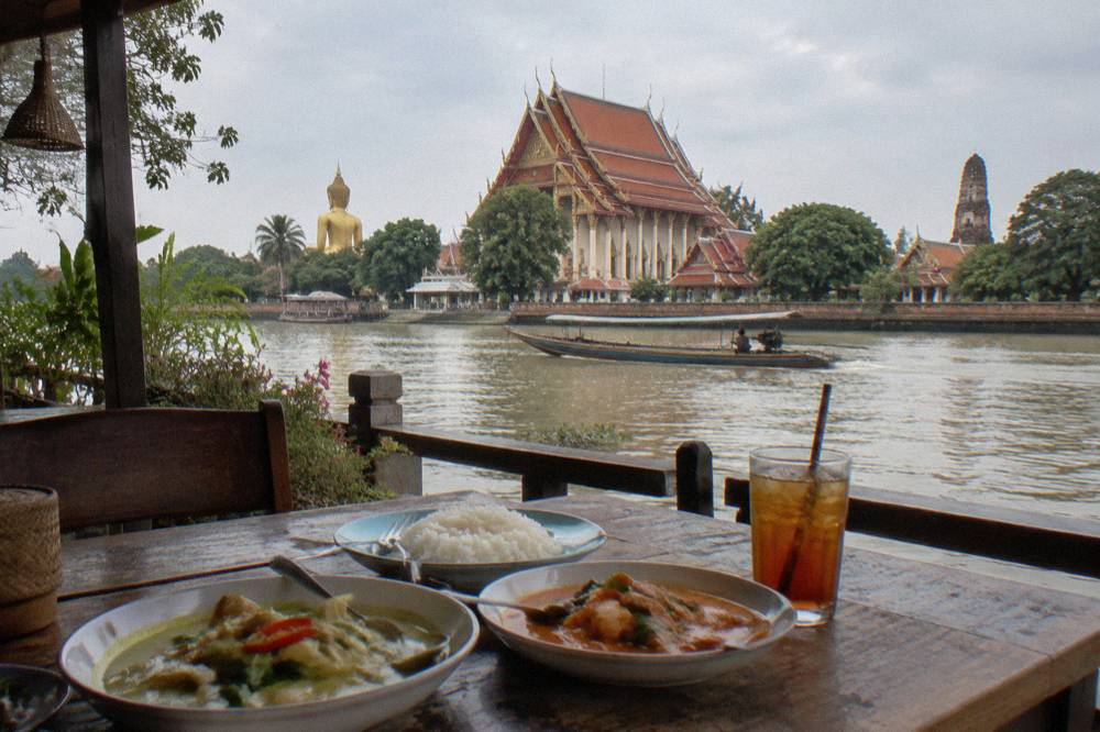 Thai lunch dishes served at a riverside restaurant table near the temples