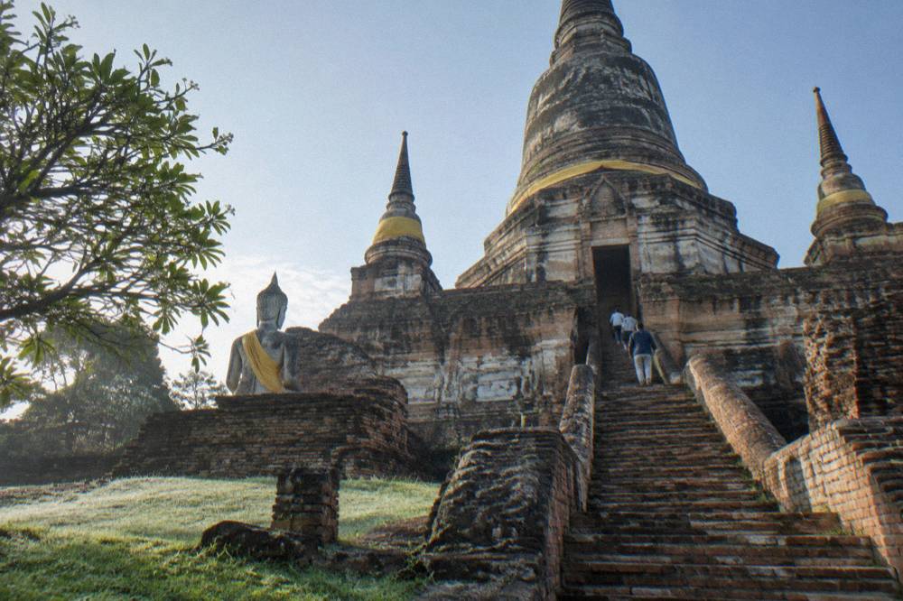 A tall brick chedi with weathered stucco rising above grass and scattered ruin stones