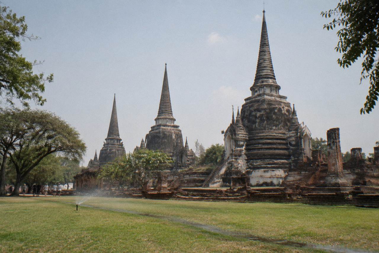 Ancient brick prangs of a ruined Ayutthaya temple standing in open grass under a wide sky