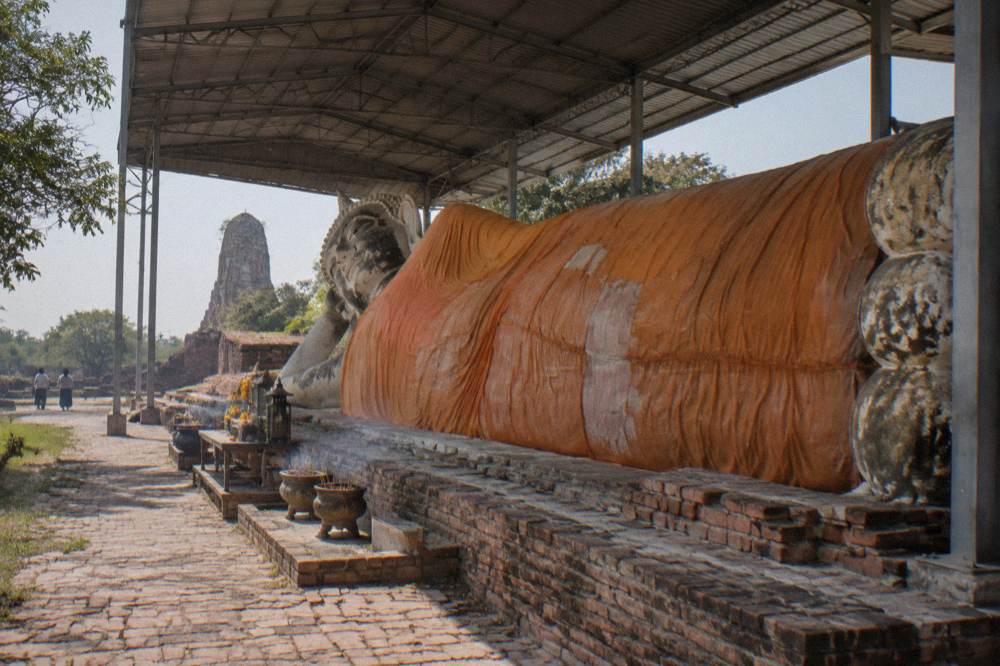 A long reclining Buddha statue resting under an open pavilion roof