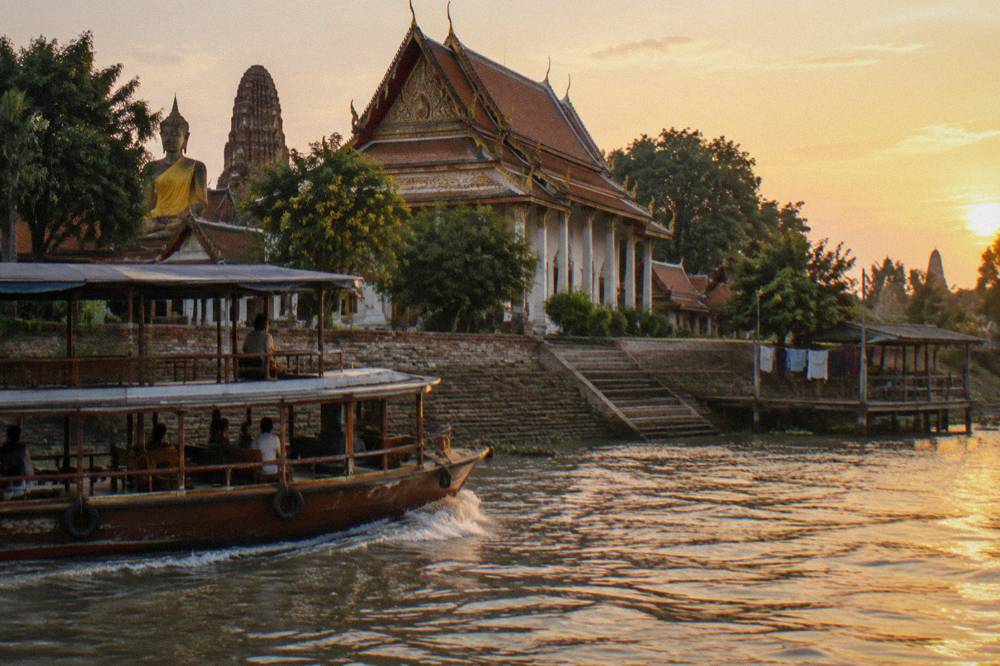 River boat cruising past temple ruins on the Chao Phraya at golden hour