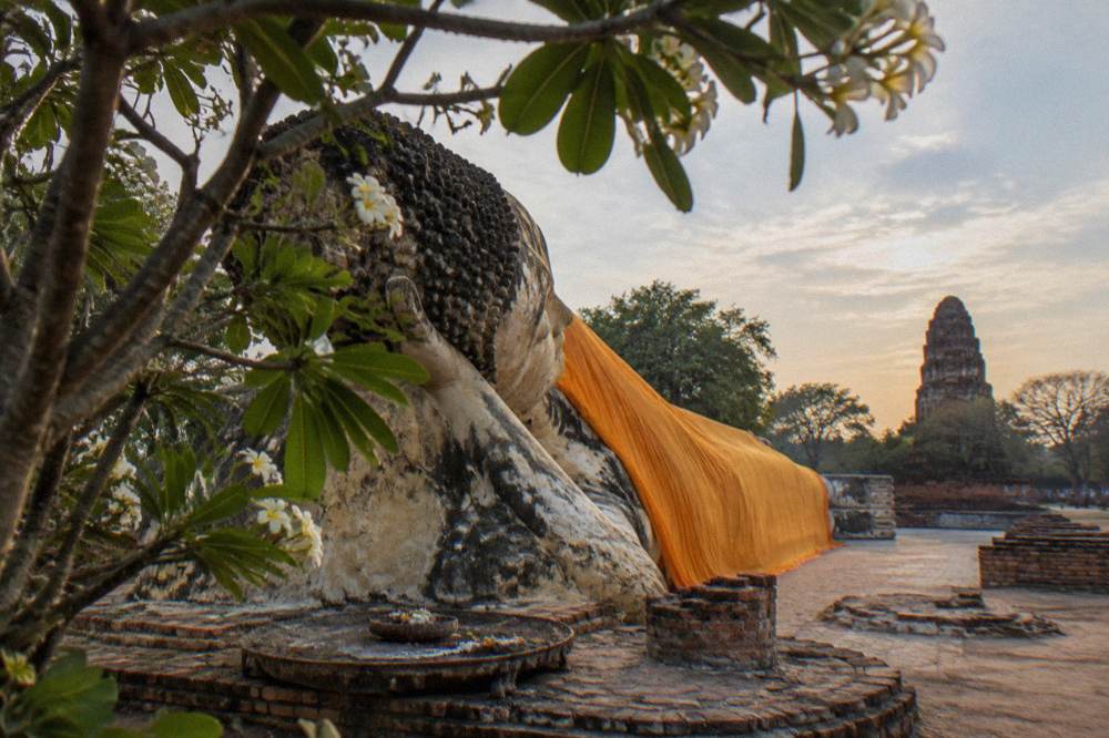 Long reclining Buddha statue resting in open-air grounds surrounded by trees