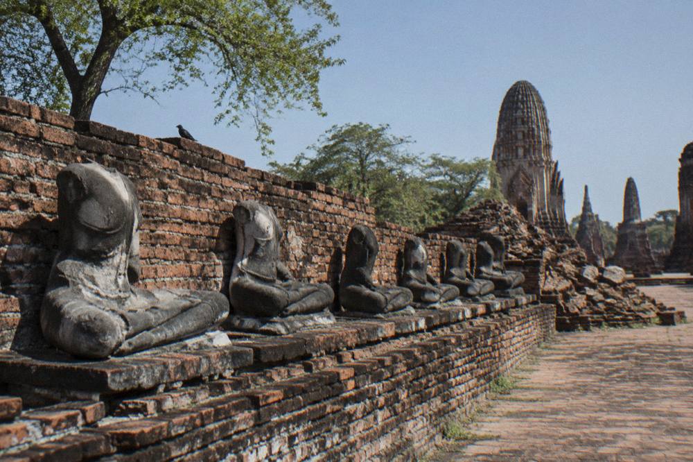 Rows of headless stone Buddha figures in weathered brick ruins under an open sky