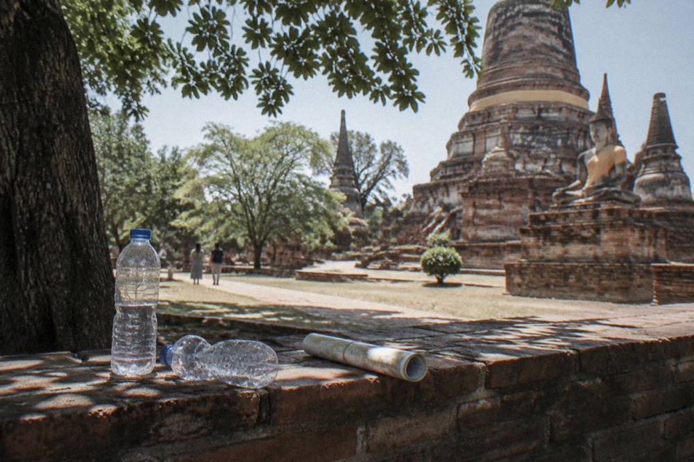 A row of bicycles leaning against a low brick wall in the shade of a large tree near temple ruins