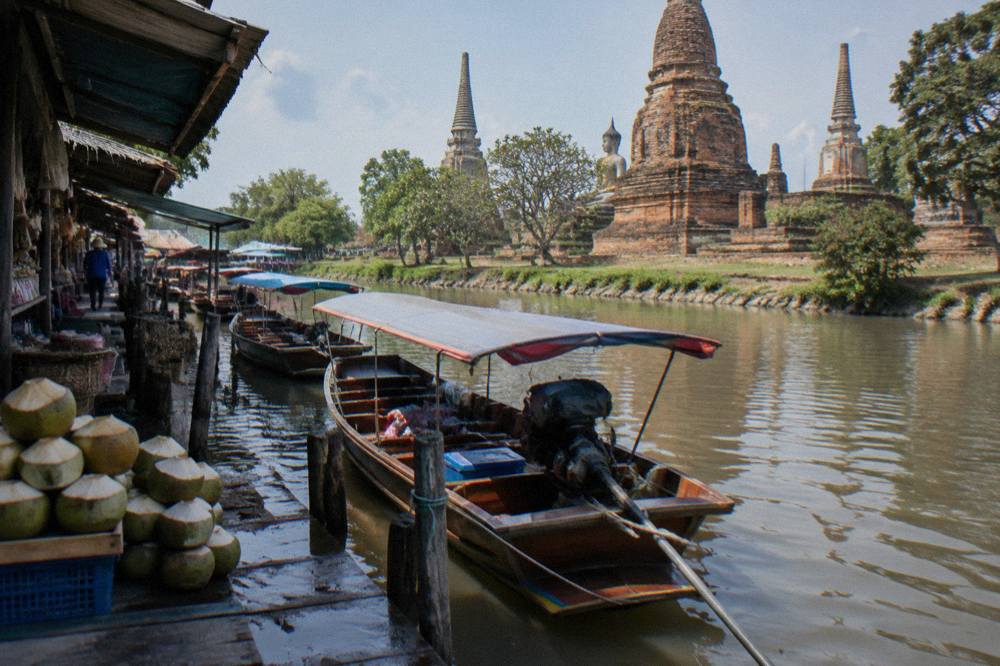 Longtail boats moored along a canal beside market stalls in Ayutthaya.
