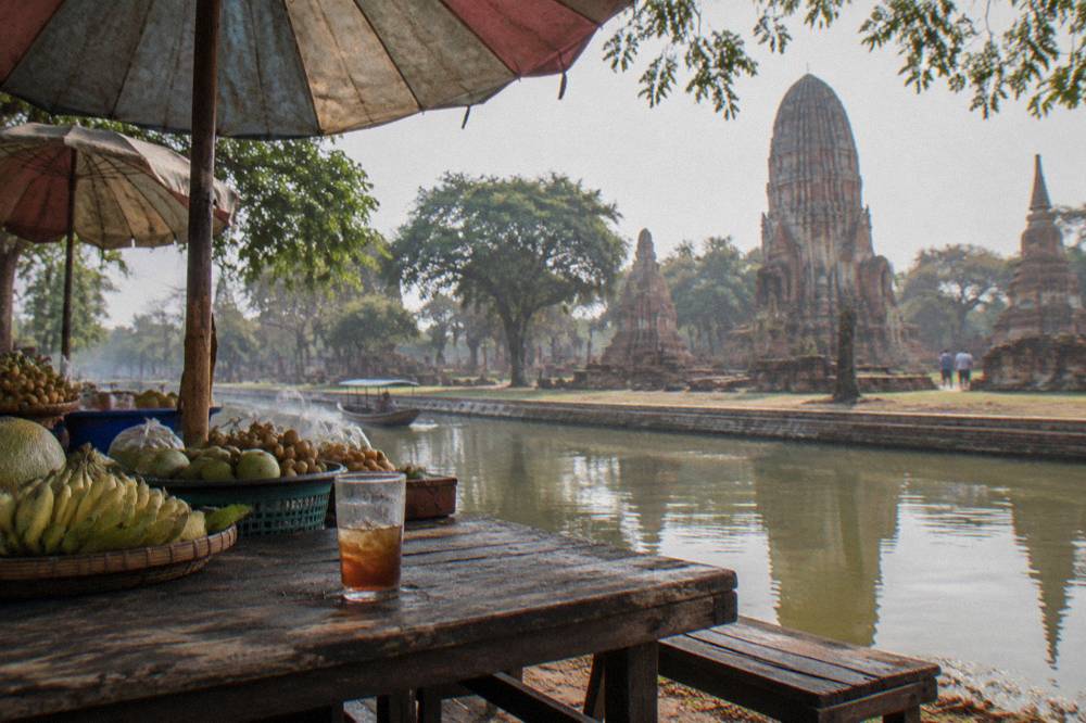 A market stall shaded by umbrellas beside a canal in a Thai floating market.