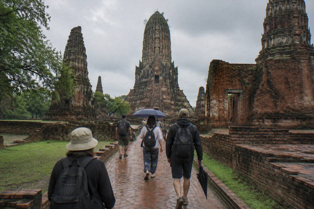 Guided tour group walking a brick path between tall temple ruins in daylight