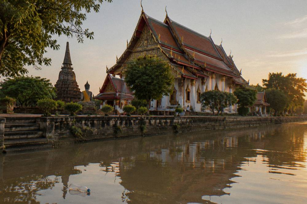 Tall central prang of a riverside temple reflected in still water at late afternoon