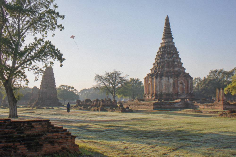 Red-brick temple ruins with pointed chedis seen across open ground in morning light