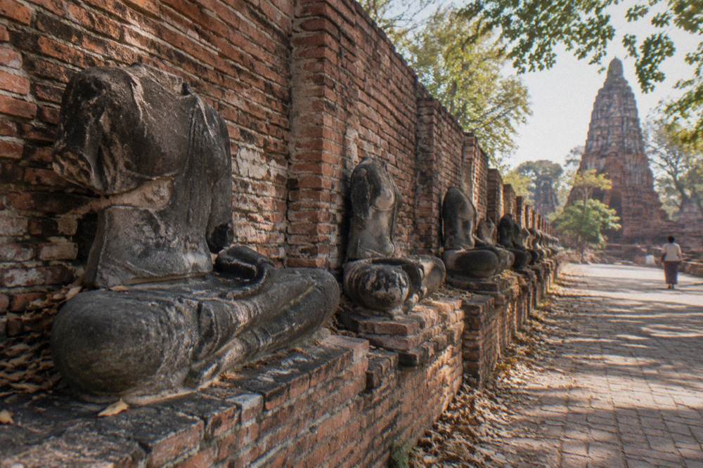 A row of weathered stone Buddha statues inside a ruined brick temple in Thailand