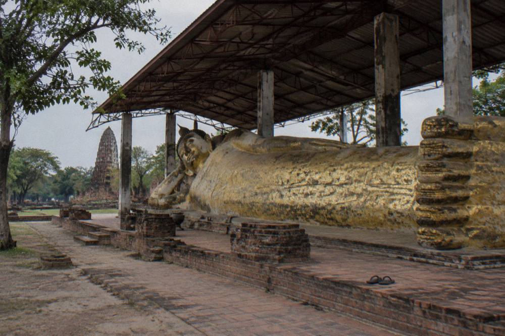 A long reclining Buddha statue resting under an open pavilion at a Thai temple