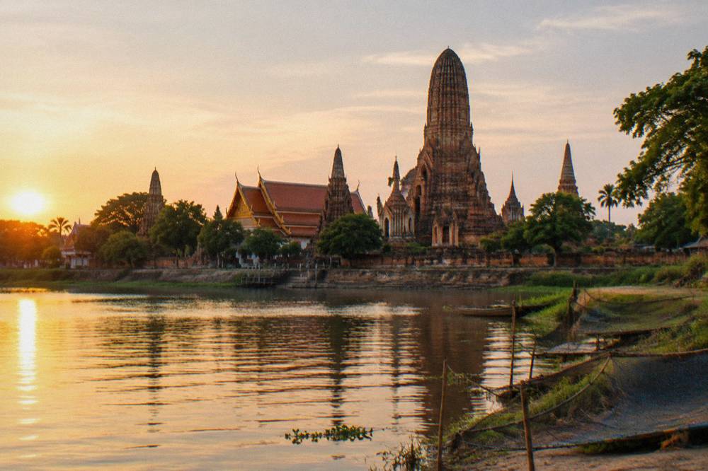 Central brick tower and surrounding smaller towers of a riverside temple seen across flat golden water