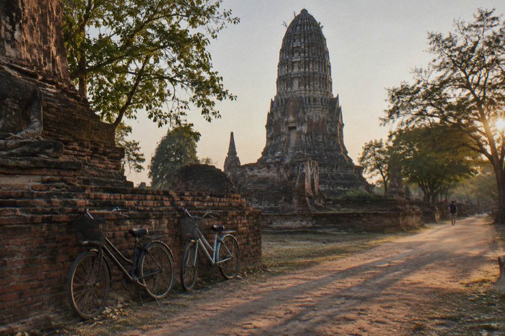 Bicycles parked outside old temple ruins with long shadows across the ground in late afternoon light