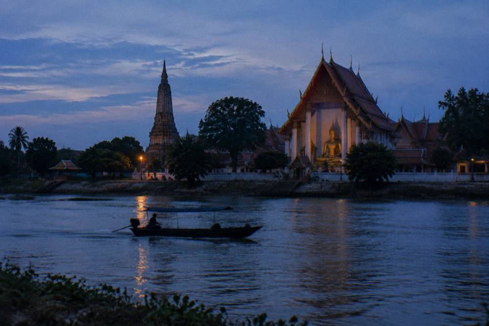 Wide river at dusk with a small boat silhouette and temple towers on the far bank