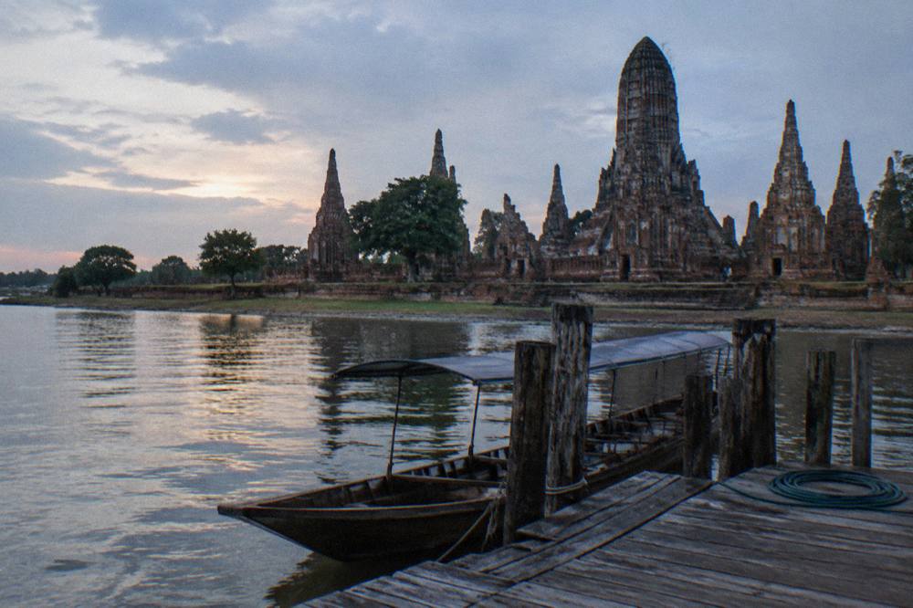 Wooden boat moored at a riverside pier with old temple walls beyond in soft evening light
