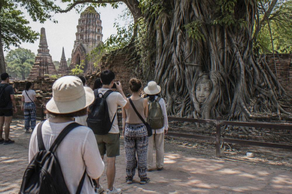 Tourists walking through the ancient brick ruins of Wat Mahathat with the iconic Buddha head in tree roots visible