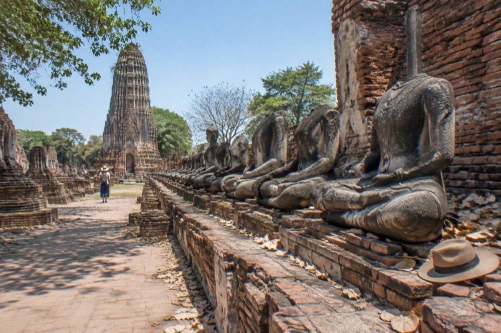 Rows of stone Buddha figures in weathered brick ruins under a clear sky