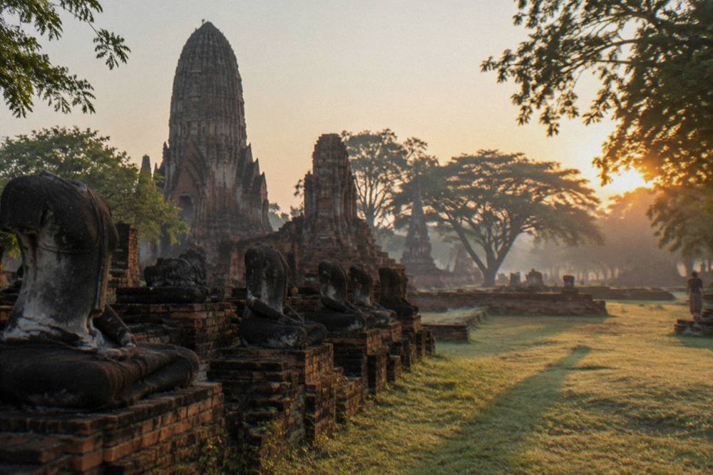 Sun rising over weathered brick temple ruins and grass in Ayutthaya historical park