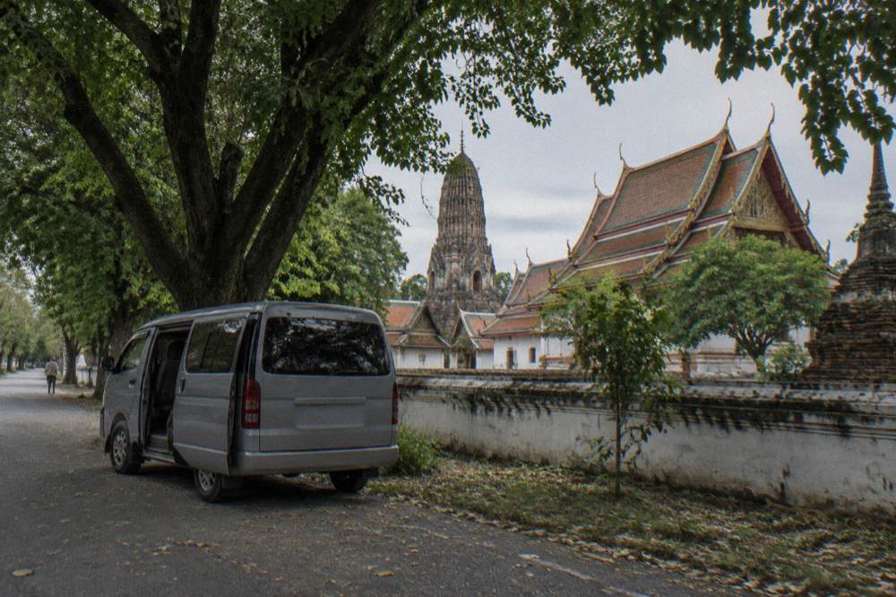 A small van parked on a shaded lane beside ancient temple ruins in Ayutthaya