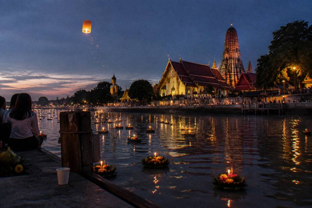 Floating lanterns and candlelight on the river beside temple ruins at a festival evening
