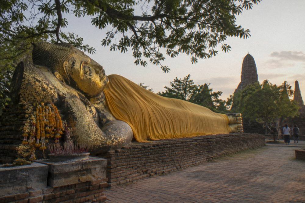 A long gilded reclining Buddha lying in the open air at a temple compound in Ayutthaya
