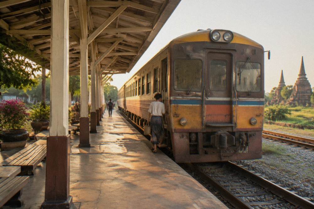 A railway platform with a train waiting beside a small provincial station under a bright sky