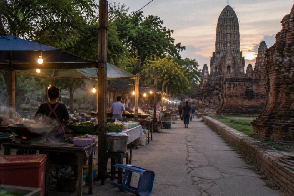 A canal-side street market with food stalls and hanging lights in the early evening