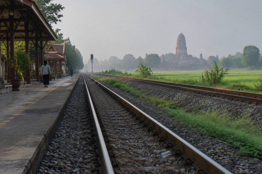 Railway tracks running beside green fields with a distant temple spire
