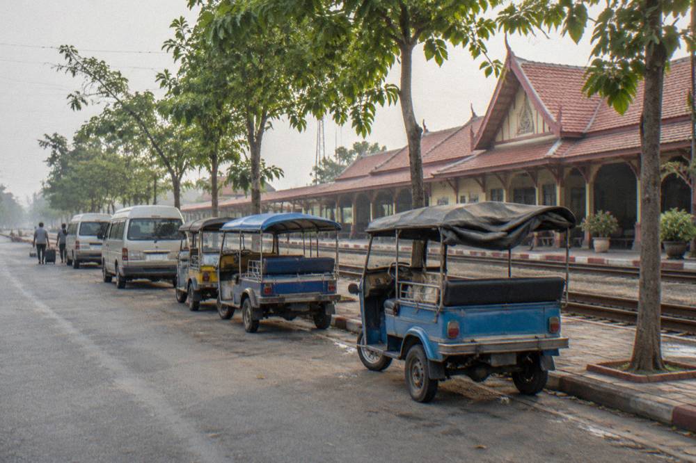 Row of parked tuk-tuks and minivans on a small-town street in morning light