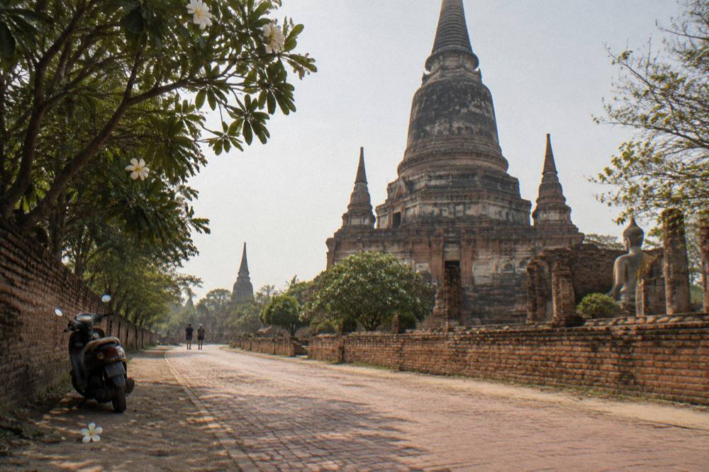 Cyclist on a quiet road passing an old brick chedi under a wide sky