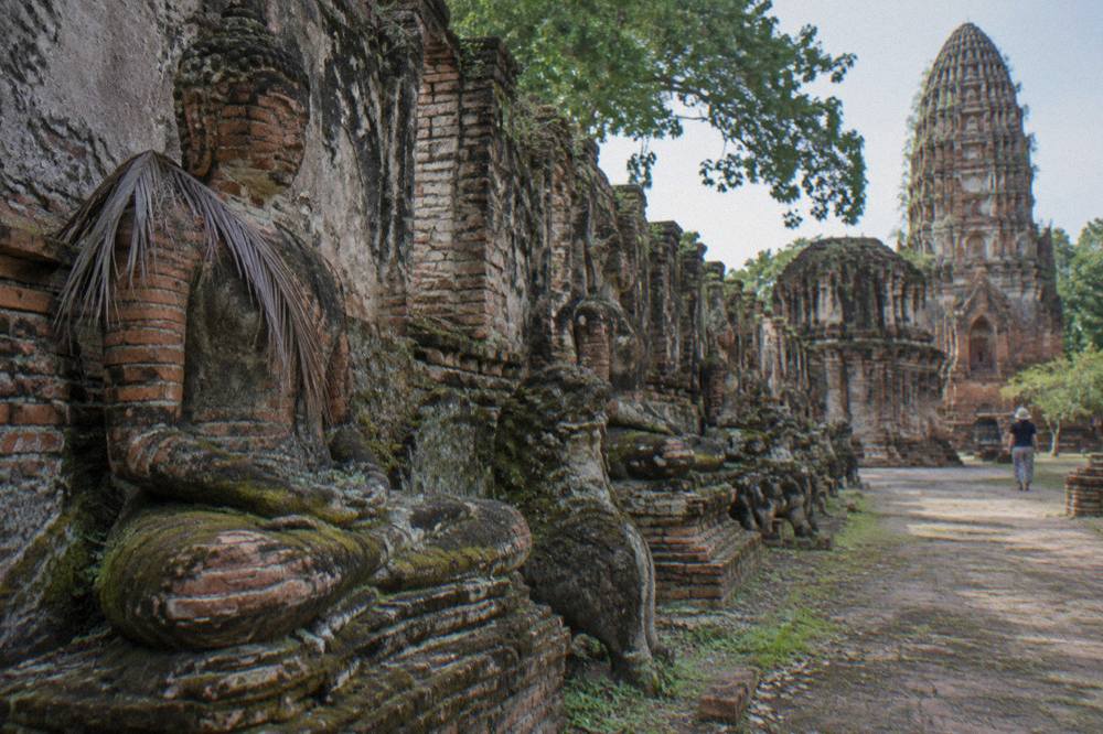 Rows of weathered stone Buddha statues lining a ruined temple wall in Ayutthaya