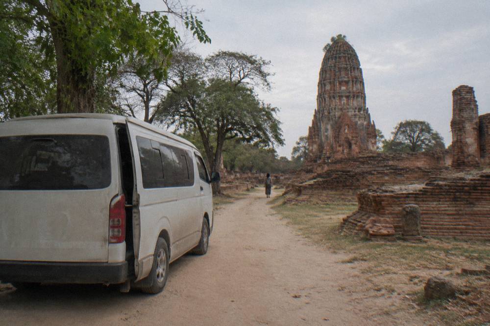 A private air-conditioned van parked on a quiet road beside ancient temple ruins