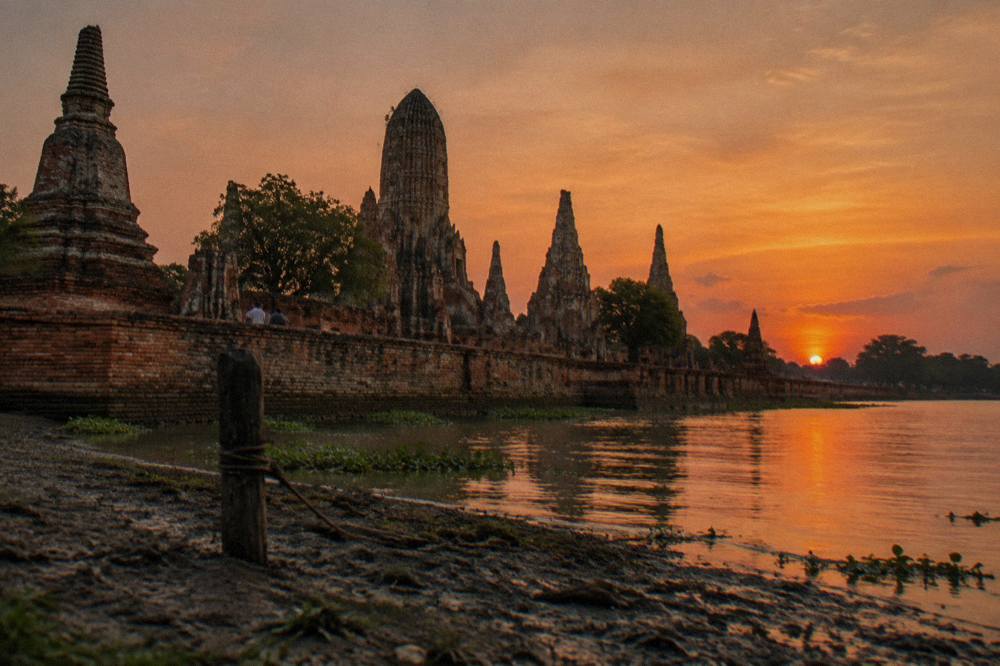 Row of brick stupas silhouetted against an orange sky beside a wide river