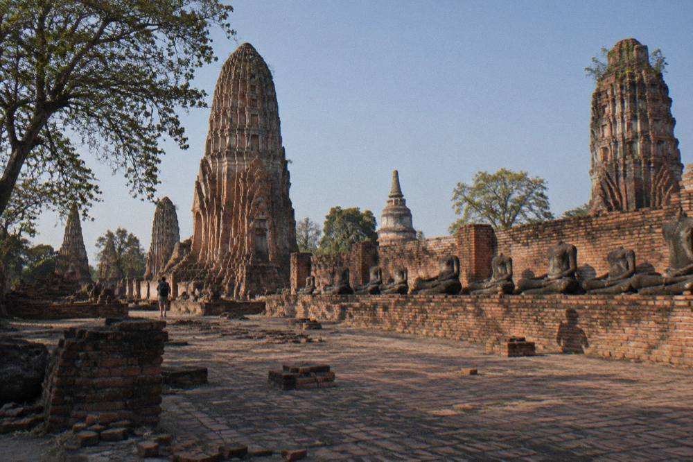 Ruined brick prangs and headless Buddha statues in a temple compound under a clear sky