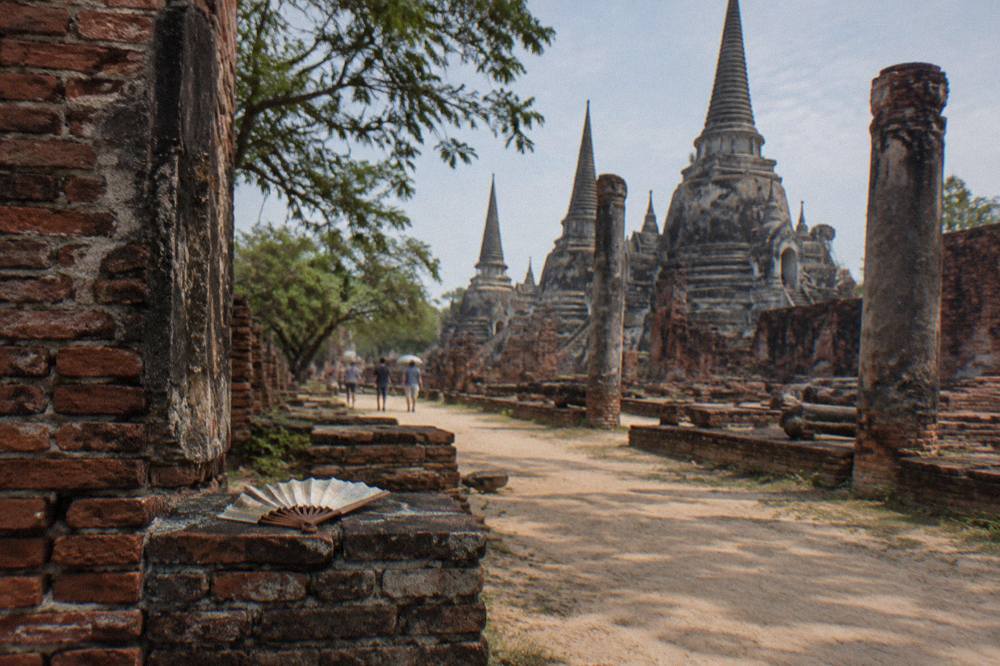 Red brick temple ruins with a sandy path and scattered stone columns in daylight