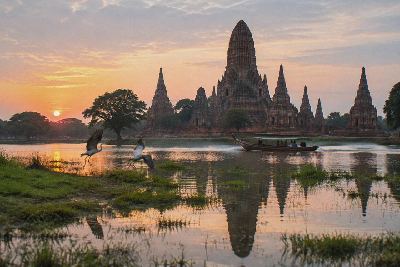 Dawn at Wat Chaiwatthanaram in Ayutthaya, the brick prang rising above flooded grass with its reflection mirrored in the still water